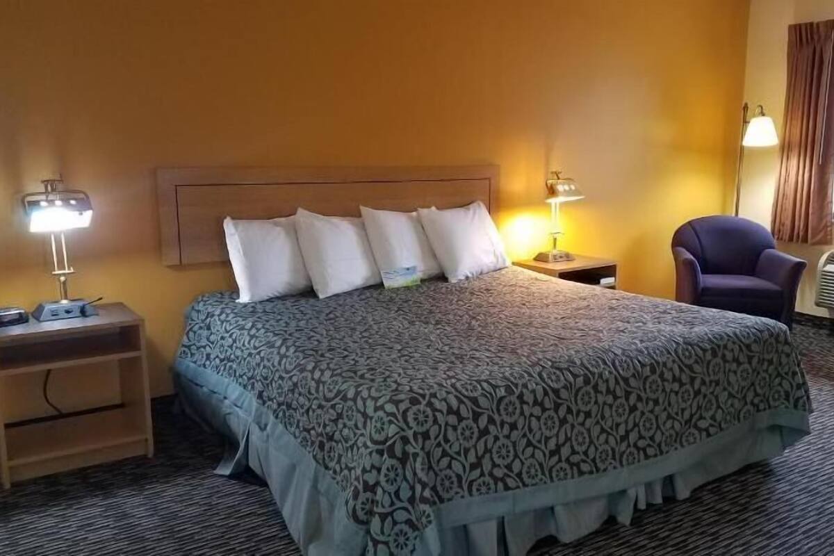 Habitación de hotel con una cama grande, dos lámparas de noche, una silla, un escritorio y una ventana con cortinas.