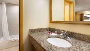 Une salle de bain avec un lavabo doté d’un plan en granit, un grand miroir et un rideau de douche.