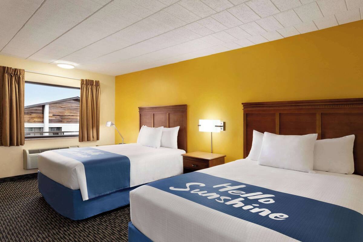 Habitación de hotel con dos camas, una ventana con cortinas, una lámpara y vista a un edificio.