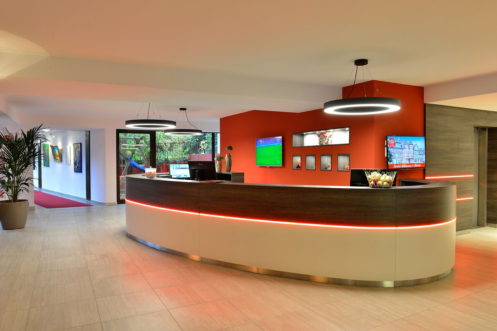 Un'area reception moderna con un banco di accoglienza curvo, una grande TV a schermo piatto e una sveglia digitale.