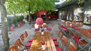 An outdoor seating area with wooden tables and red chairs, surrounded by trees and a building with a red facade. - Michel Hotel Wetzlar (Wetzlar)