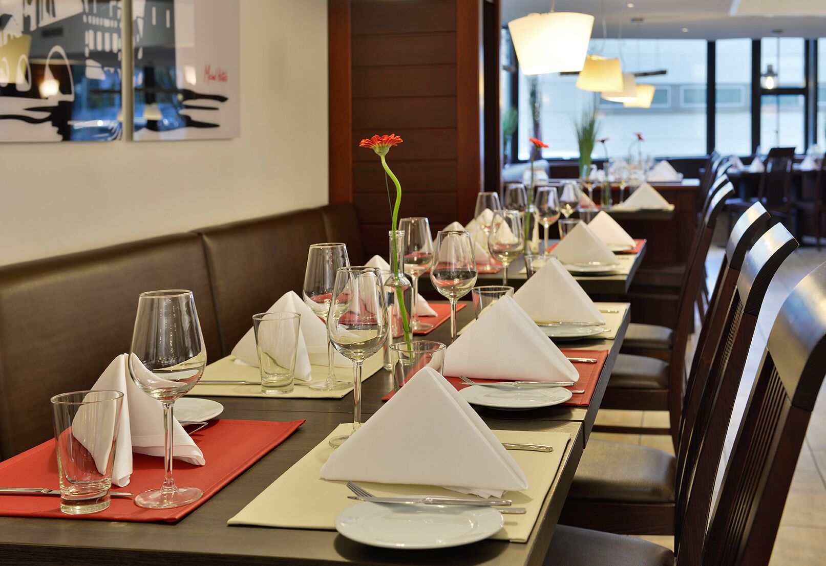 A restaurant with a long table set for dining, featuring neatly arranged plates, glasses, and napkins.