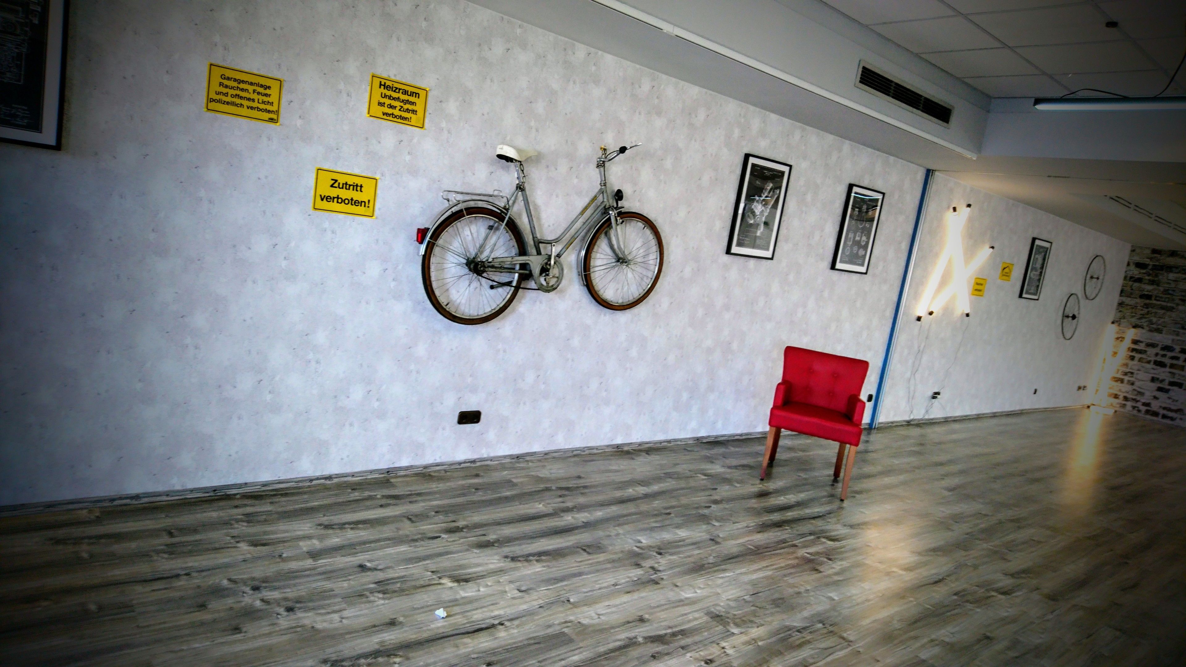 Un pasillo con suelo de madera, una silla roja y una bicicleta colgada en la pared.