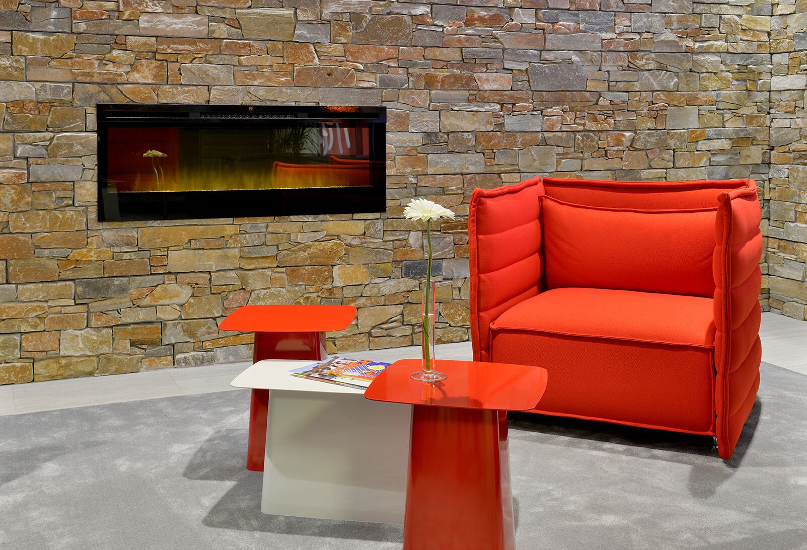 Een modern interieur met een stenen muur, een flatscreen televisie, een rode fauteuil en een klein tafeltje met een tijdschrift.