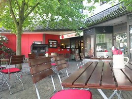 Un espacio al aire libre con mesas y sillas de madera, una pared roja y un letrero que dice 'Rsy Lahn-Dill'.