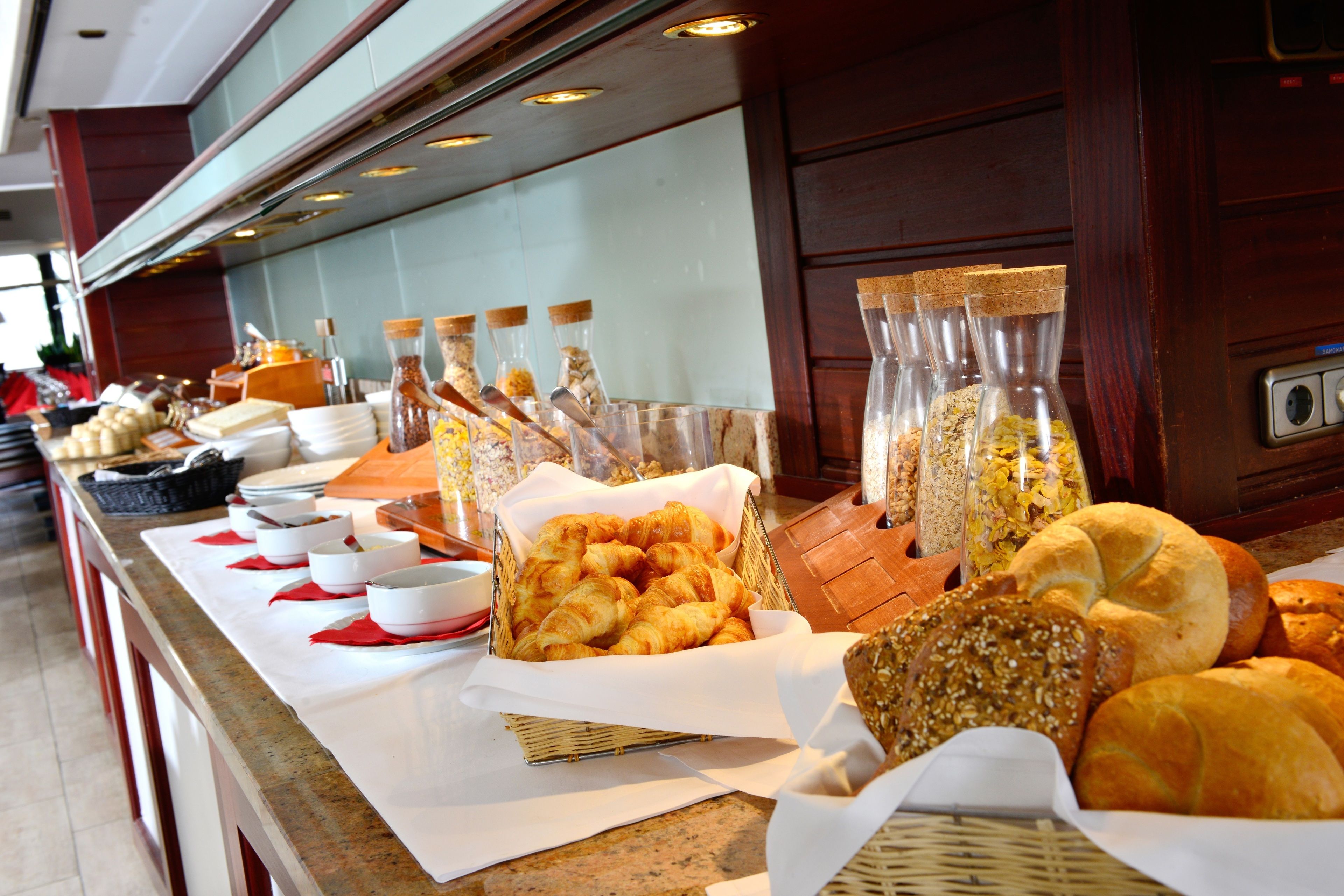 A buffet with various food items, including bread and pastries, arranged on a counter with serving utensils and containers.
