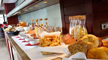 A buffet with various food items, including bread and pastries, arranged on a counter with serving utensils and containers.