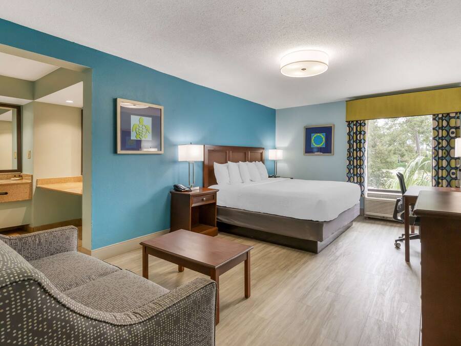 A hotel room with a bed, a desk, a chair, a nightstand, and a mirror.