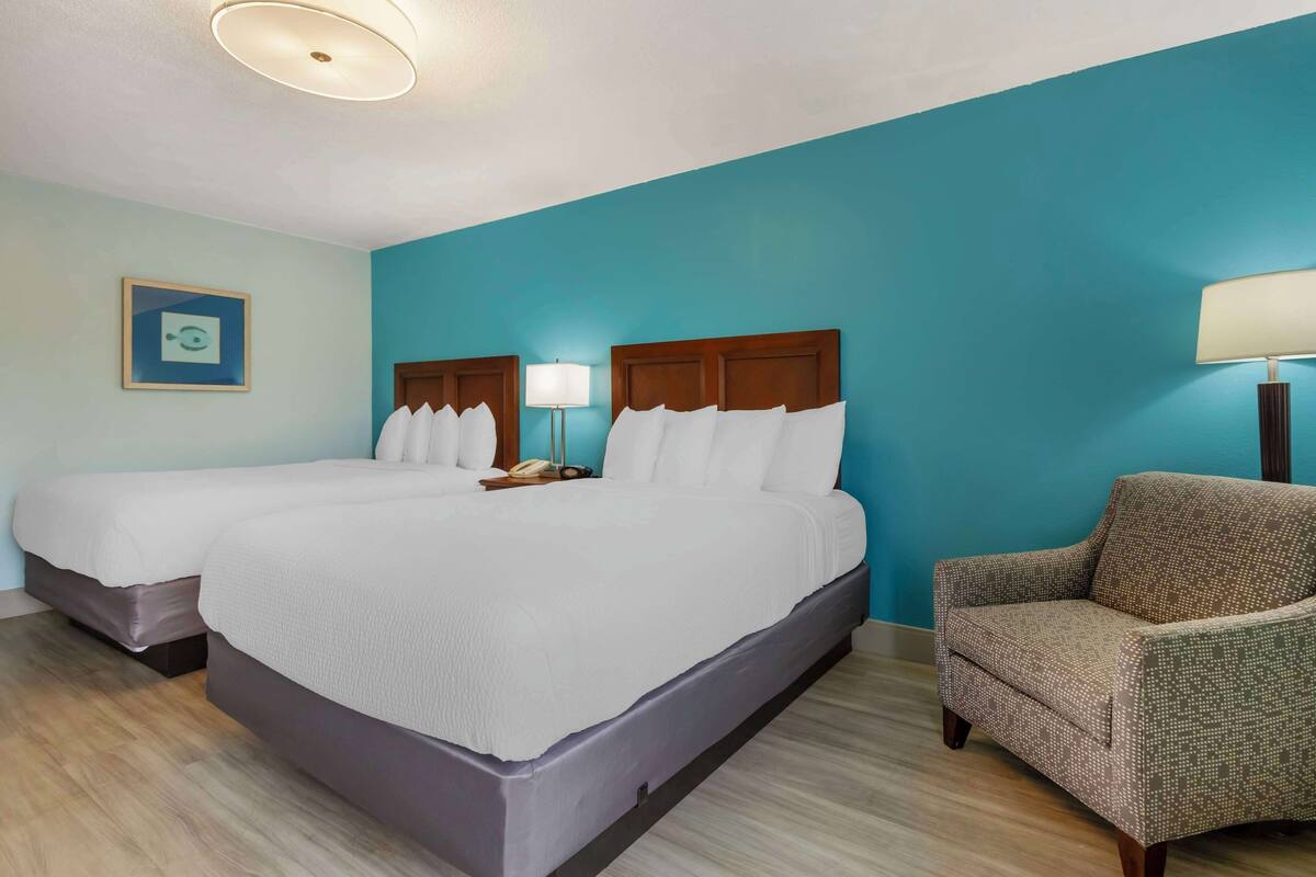 A hotel room with two beds, a chair, and a nightstand with a lamp.