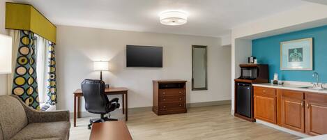 A hotel room with a bed, a desk, a chair, a dresser, a television, a microwave, and a sink.