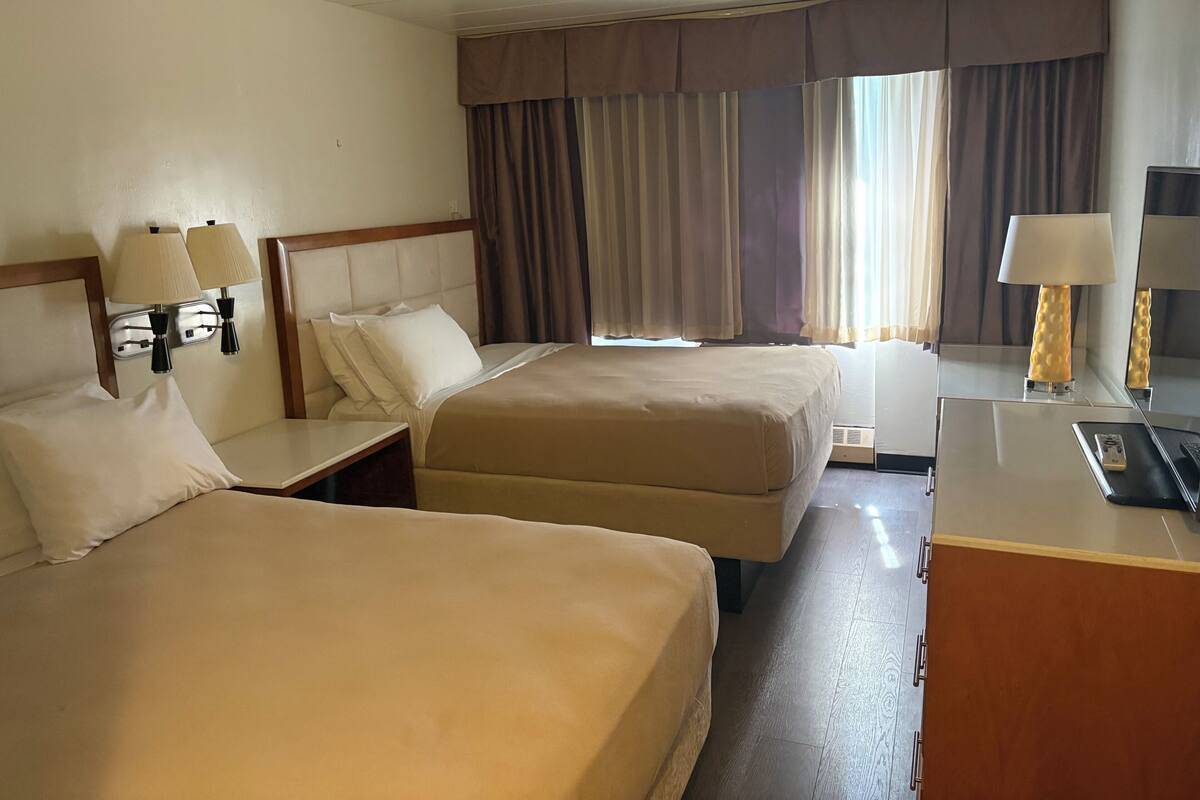 Une chambre d’hôtel avec deux lits, un bureau, une lampe et une fenêtre avec des rideaux.