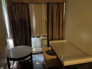 Ein Zimmer mit einem runden Tisch, einem rechteckigen Tisch und einem Fenster mit Vorhängen.
