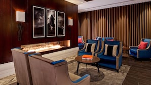 A modern lounge area with a fireplace, blue upholstered chairs, and wall-mounted artwork.