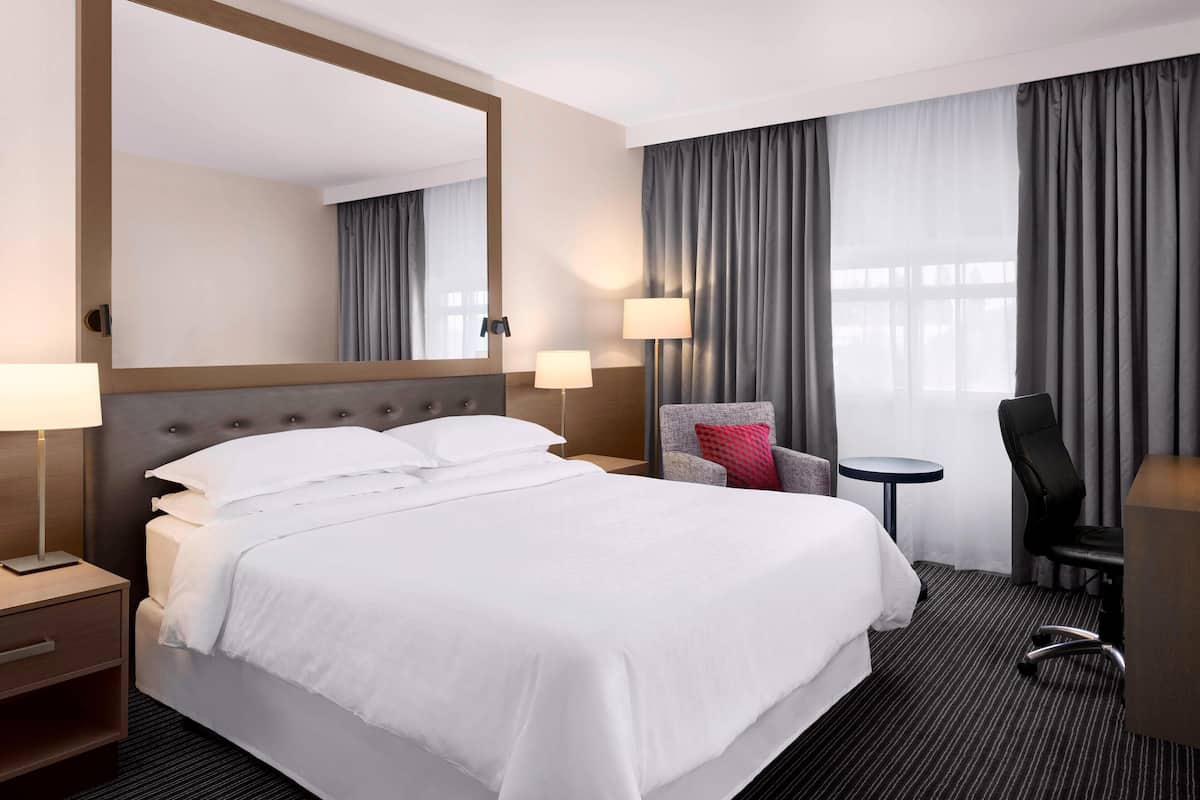 Una habitación de hotel con una cama grande, un escritorio, una silla, una mesita pequeña y un espejo amplio.