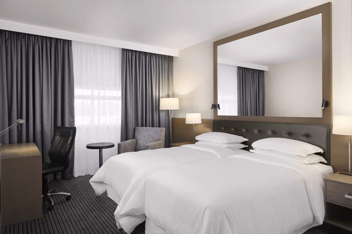 Una habitación de hotel con una cama grande, un escritorio, una silla, una mesita pequeña y un espejo amplio.