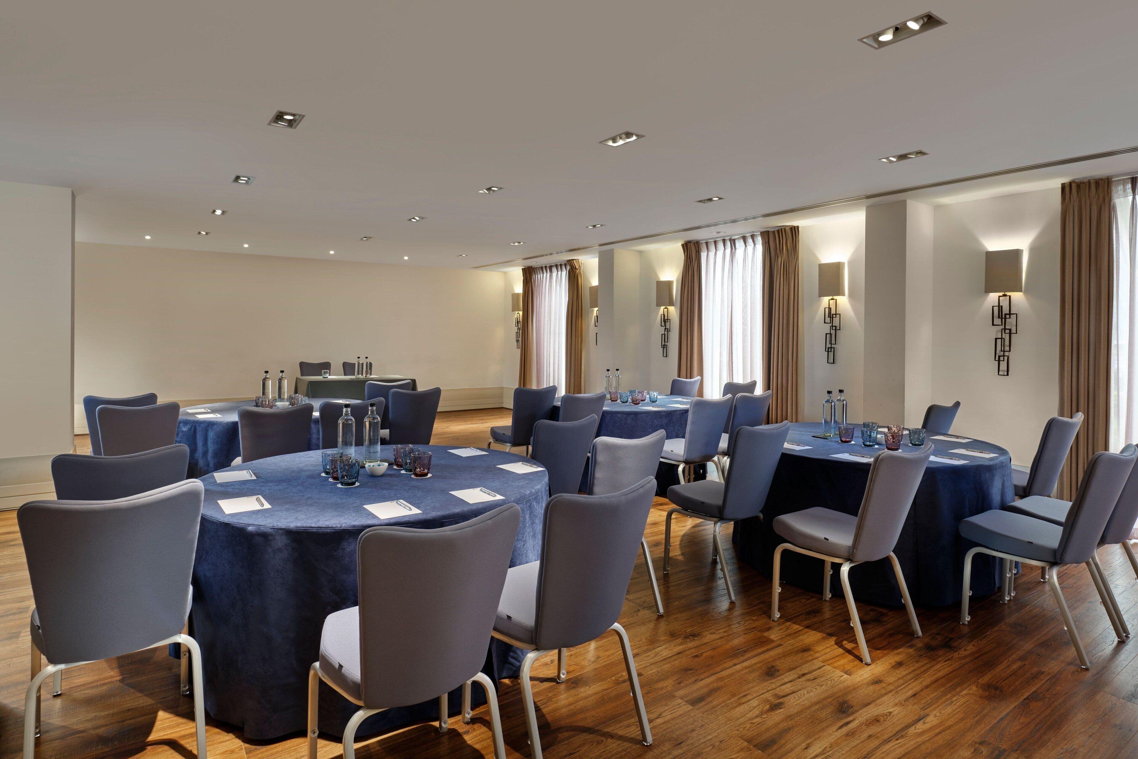 A conference room with round tables, chairs, and a wooden floor.