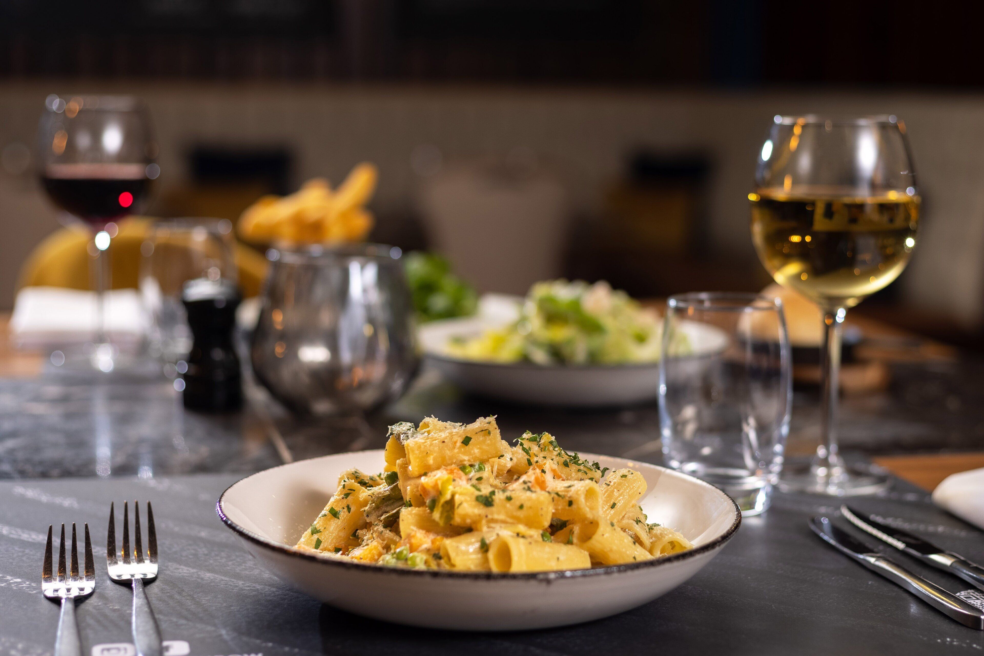 Une table à manger avec une assiette de pâtes, des verres à vin et des couverts.