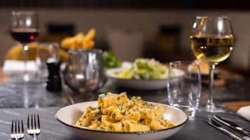 A dining table with a plate of pasta, wine glasses, and cutlery.