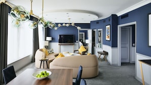 A modern living room with a sofa, a dining table with a bowl of fruit, and a television.