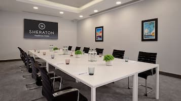 A conference room with a white table, black chairs, and a logo on the wall.