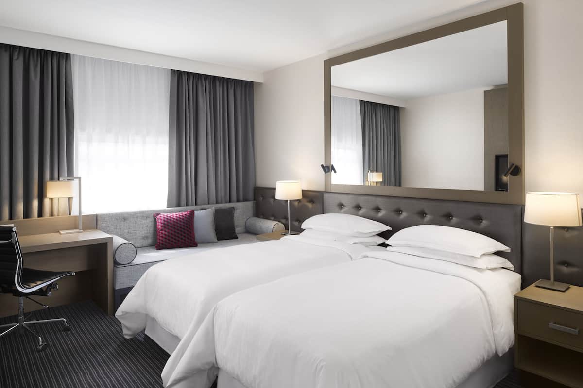 Habitación de hotel con una cama grande, dos mesitas de noche, un escritorio con silla y un espejo amplio.
