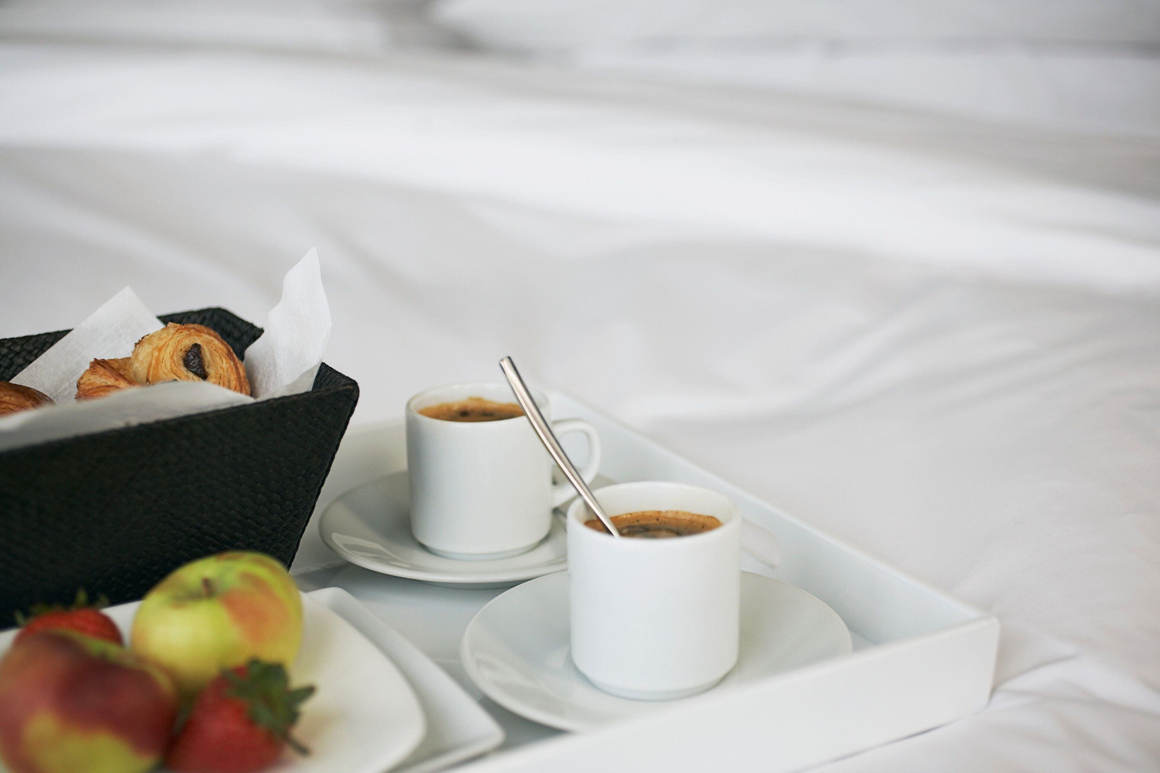 Un desayuno con croissants, tazas de café y fresas sobre una cama.