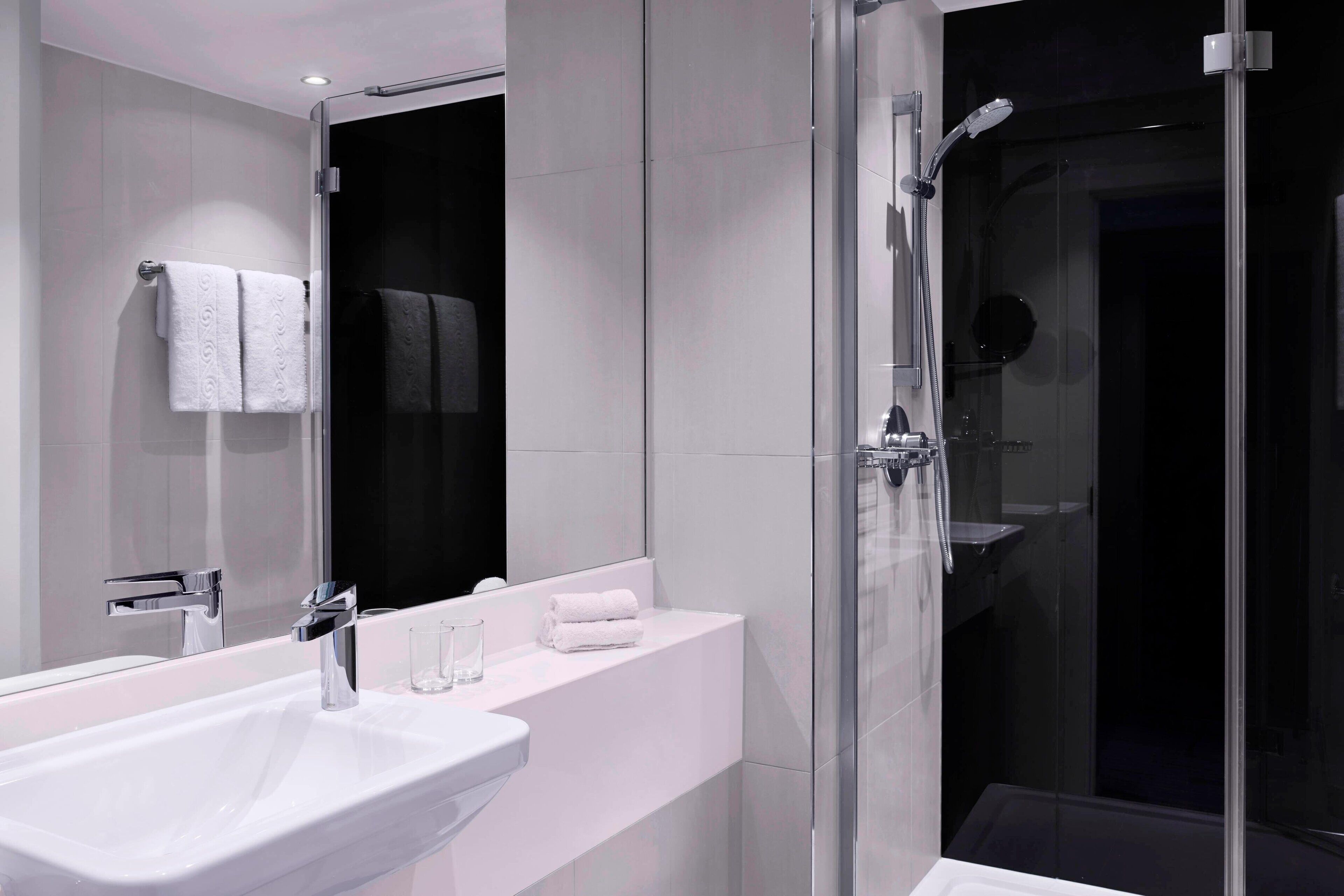 A modern bathroom with a glass-enclosed shower, a white sink, and a mirror above the sink.