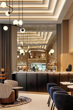 A bar area with a modern design, featuring a bar counter, seating, and hanging pendant lights. - Sheraton Heathrow Hotel (West Drayton)