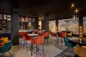 Un área de bar moderna con sillas rojas y aguamarina, una barra con botellas y un gran mapa mundial en la pared.