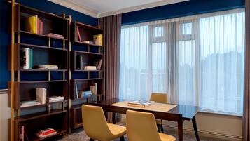 Una habitación con una estantería de madera, una mesa con sillas y un amplio ventanal con cortinas traslúcidas.