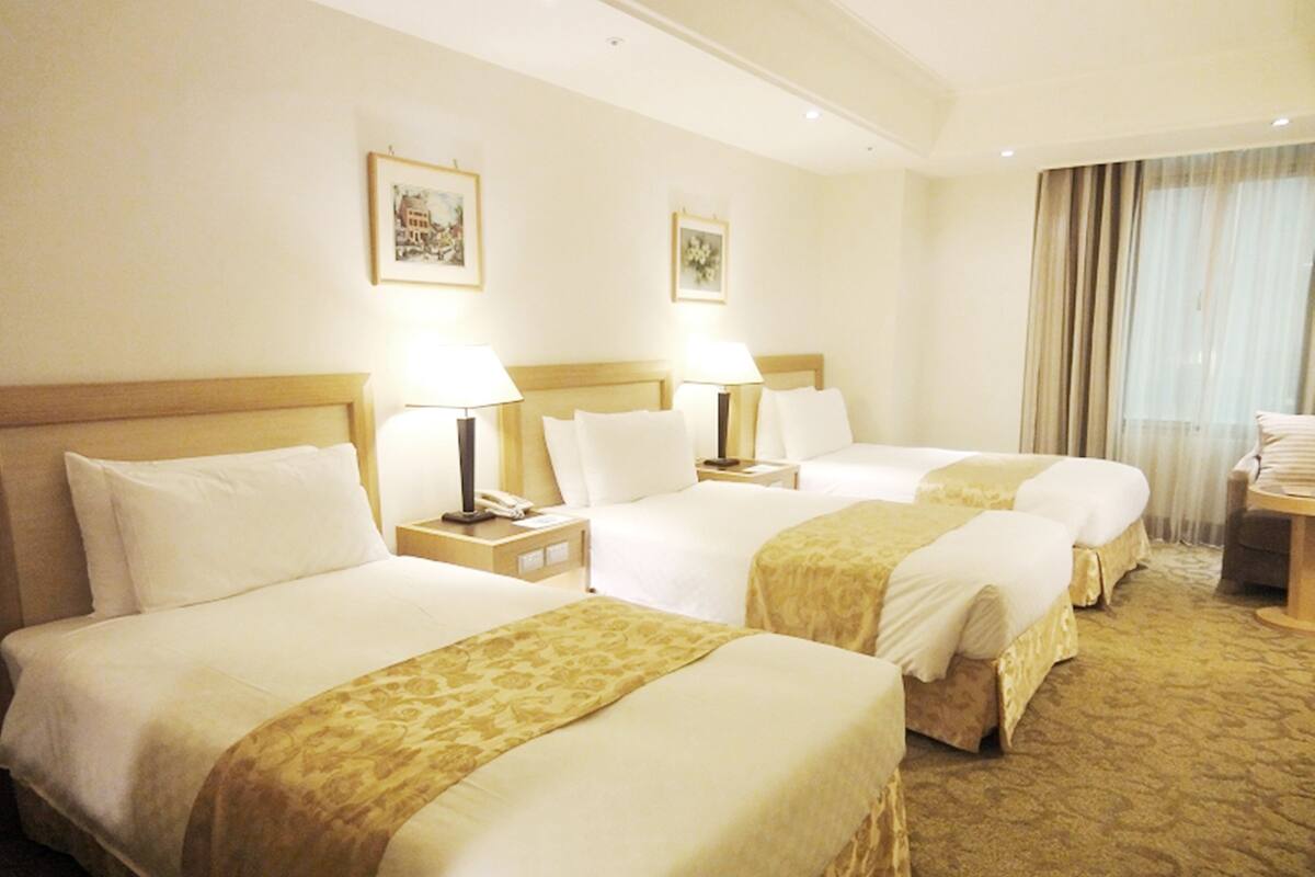 A hotel room with three beds, each with a headboard, bedside tables with lamps, and a carpeted floor.