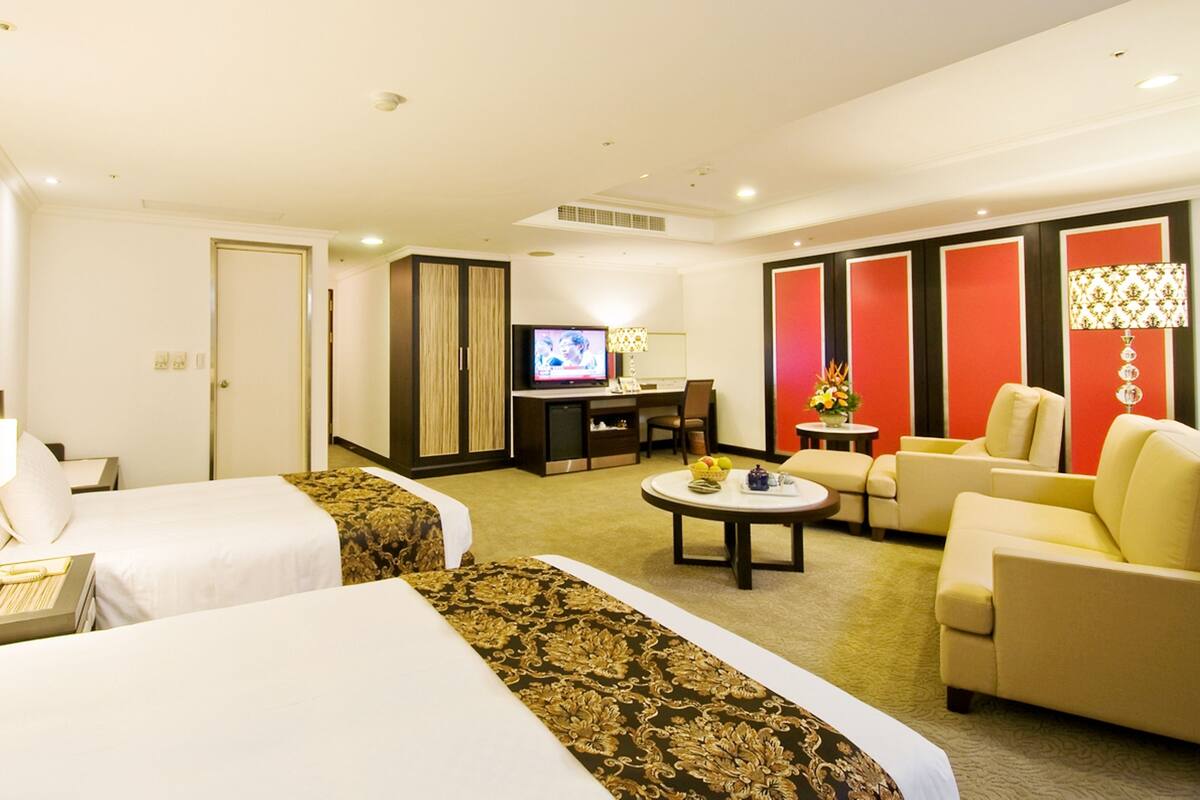 A hotel room with two beds, a TV, a desk, a sofa, and a coffee table.