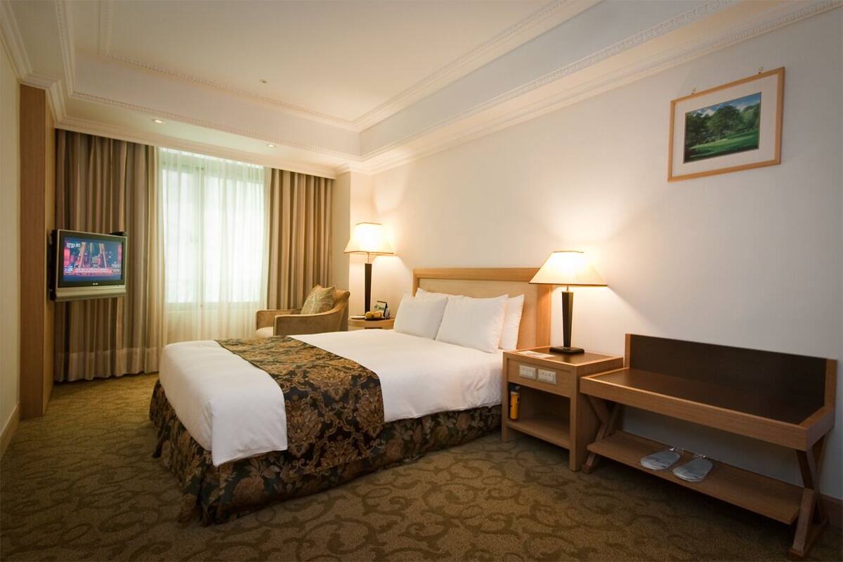 A hotel room with a large bed, two bedside tables with lamps, a TV, a chair, and a desk with a chair.