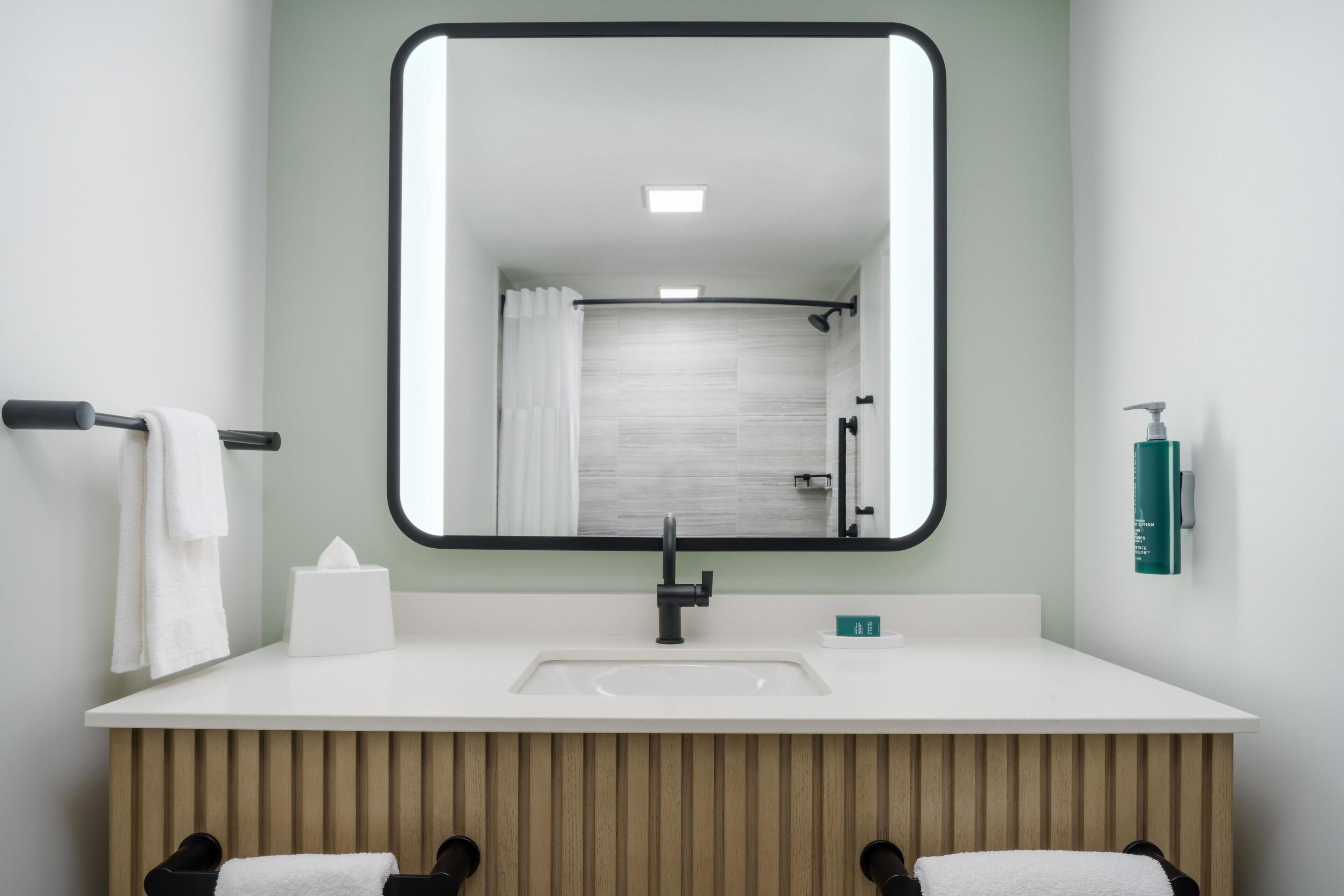 A modern bathroom with a large mirror, white sink, and wooden vanity.