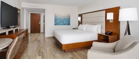 A hotel room with a bed, a desk, a chair, a TV, and a painting on the wall.