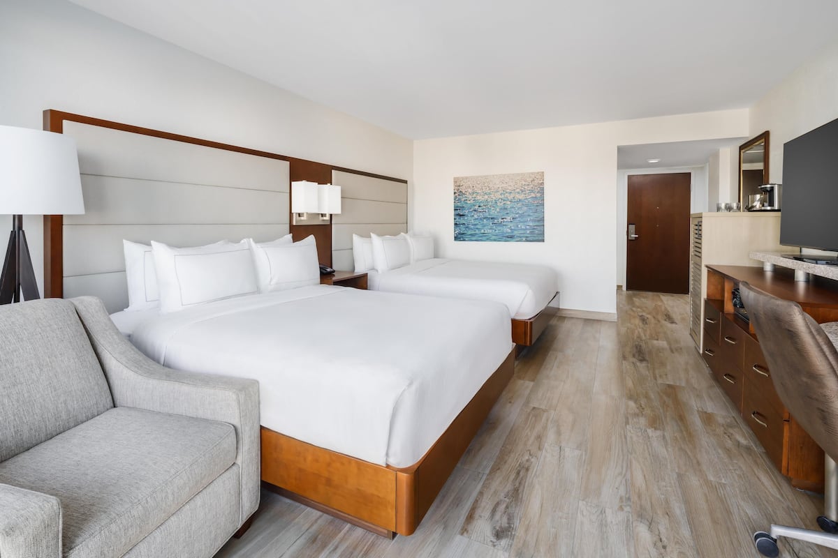 A hotel room with a large bed, a sofa, a desk with a chair, a TV, and a painting on the wall.