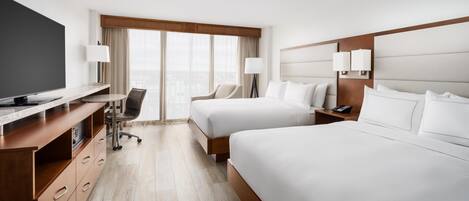 A hotel room with a TV, desk, two beds, a chair, and a view of the city.