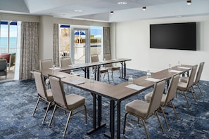 A conference room with a large table, chairs, a screen, and a view of the ocean.