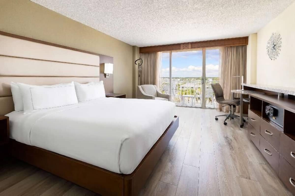 A hotel room with a large bed, a desk, a chair, and a view of the city.