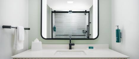 A modern bathroom with a large mirror, white sink, and wooden vanity.
