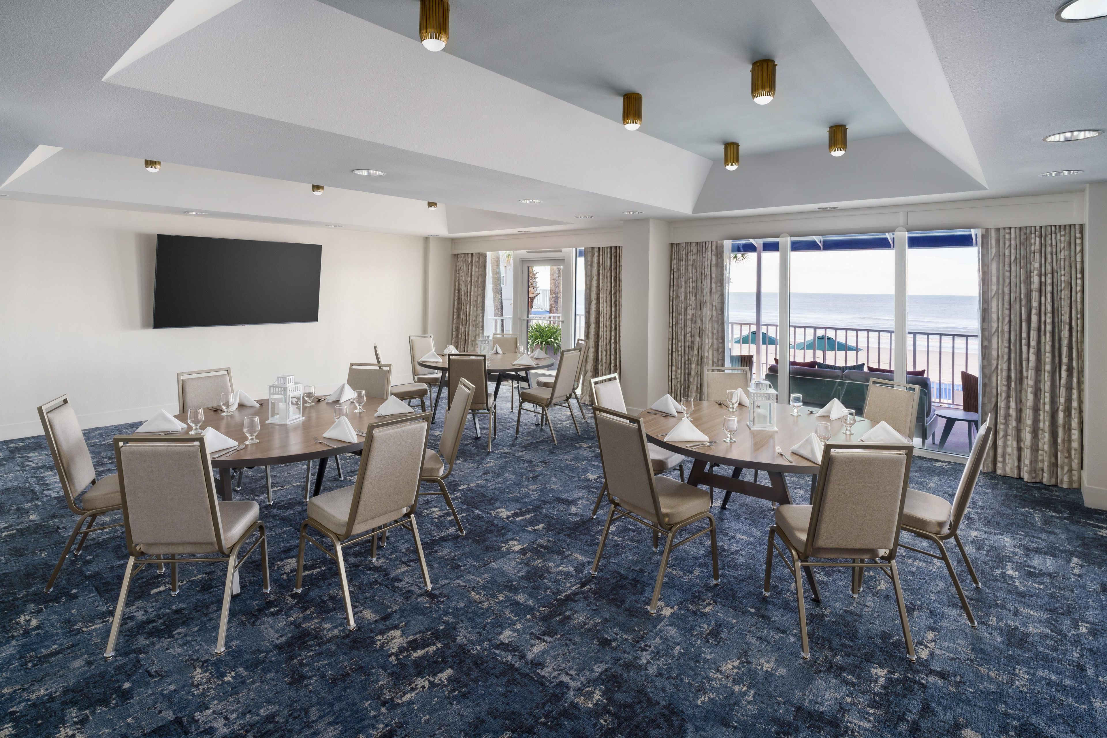 Un salón de conferencias de hotel con varias mesas, sillas y una pantalla grande.