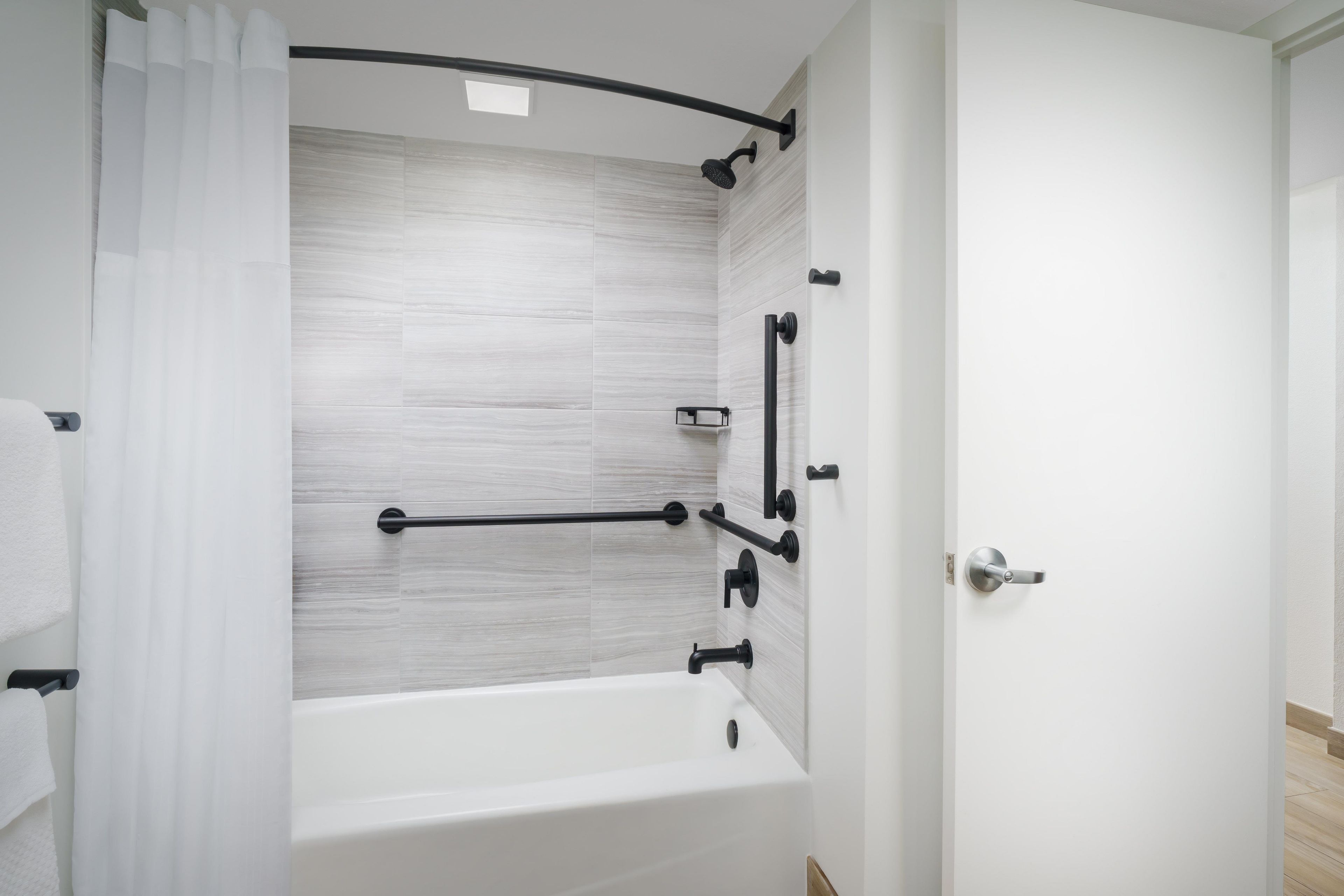 A modern bathroom with a white bathtub, a shower area, and a door with a handle.