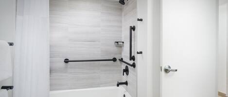 A modern bathroom with a white bathtub, a shower area, and a door with a handle.