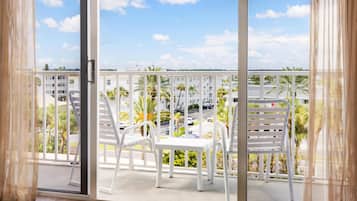 Un balcón con sillas y una mesa blancos, con vistas a una zona residencial con palmeras y edificios.