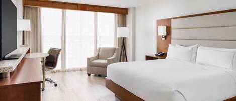 Une chambre d’hôtel avec un grand lit, un bureau avec un ordinateur, une chaise, une télévision et une fenêtre avec des rideaux.
