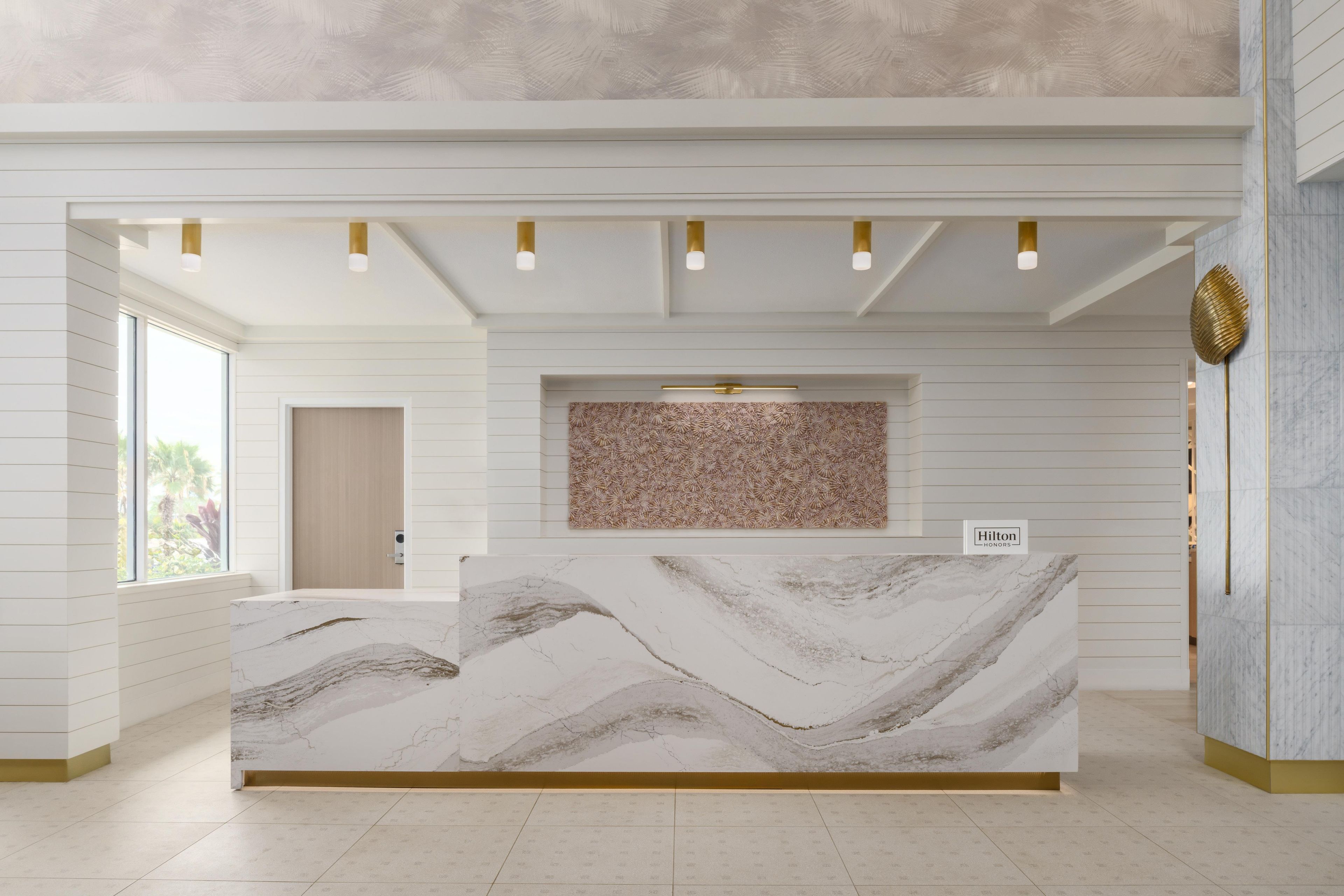 A hotel reception desk with a marble top, a patterned wall above it, and a door in the background.