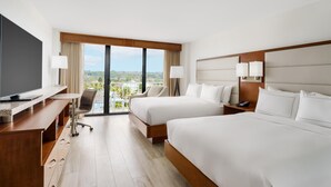 Ein Hotelzimmer mit zwei Betten, einem Schreibtisch, einem Fernseher und Blick auf die Stadt.
