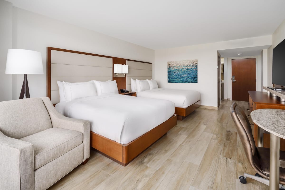 A hotel room with a large bed, a sofa, a desk, and a painting on the wall.