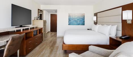 A hotel room with a bed, a desk with a flat-screen TV, a chair, a painting on the wall, and a wooden headboard.