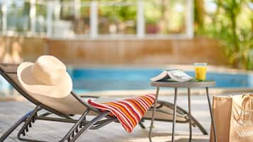 A poolside lounge chair with a hat and a striped towel, a glass of orange juice, and a bag on a small table.